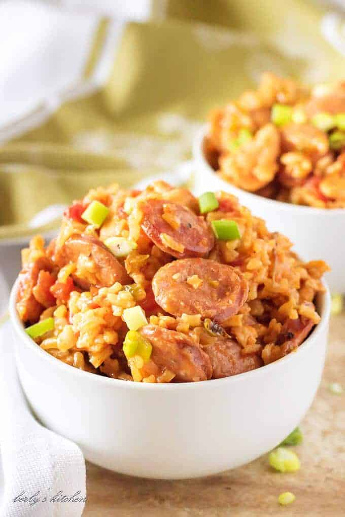 Close up view of sausage and chicken jambalaya in two white bowls with scattered green onions.
