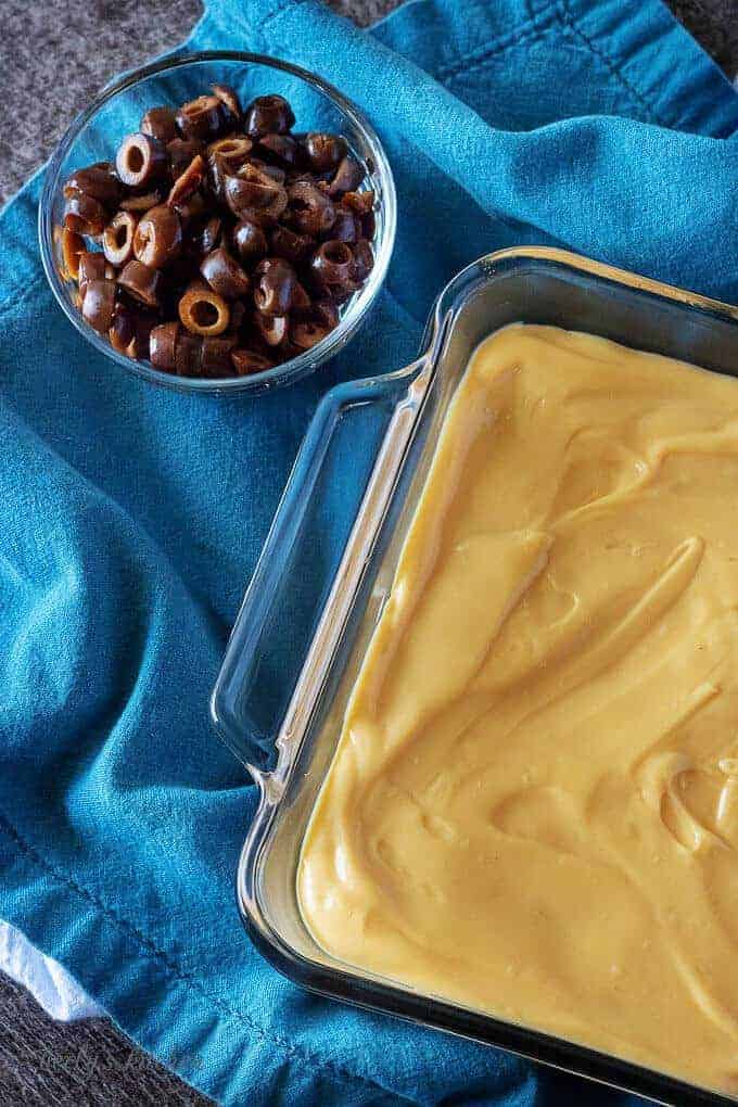 A top down picture of the 7 layer dip being made. The second layer, nacho cheese, has been put on top of the refried beans.