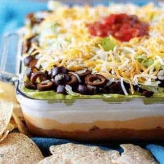 The finished 7 layer dip topped with salsa, in a large casserole dish on a blue towel.
