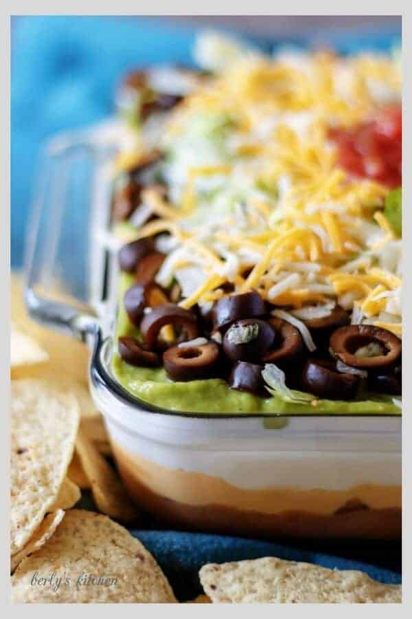 A close-up photo of the finished 7 layer dip loaded with cheese, olives, and sour cream.