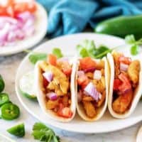 A close-up picture of the finished chicken soft tacos garnished with toppings likes cilantro, red onion, and diced tomatoes.
