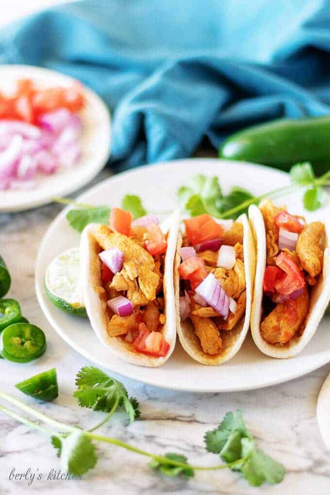 A close-up picture of the finished chicken soft tacos garnished with toppings likes cilantro, red onion, and diced tomatoes.