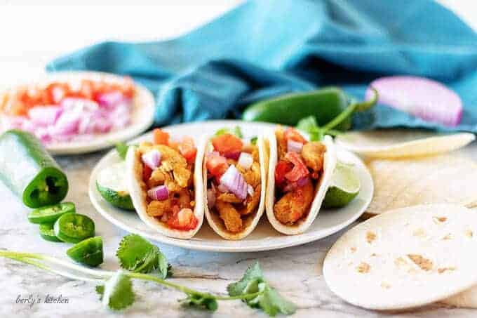 Three finished instant pot street tacos on a white plate topped with onions and tomatoes.