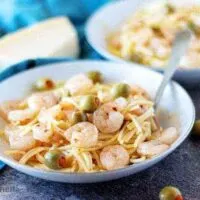 The finished shrimp and pasta in two white bowls garnished with green olives.