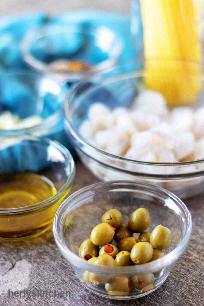 A close-up photo of the ingredients like olive oil, green olives, and peeled shrimp.