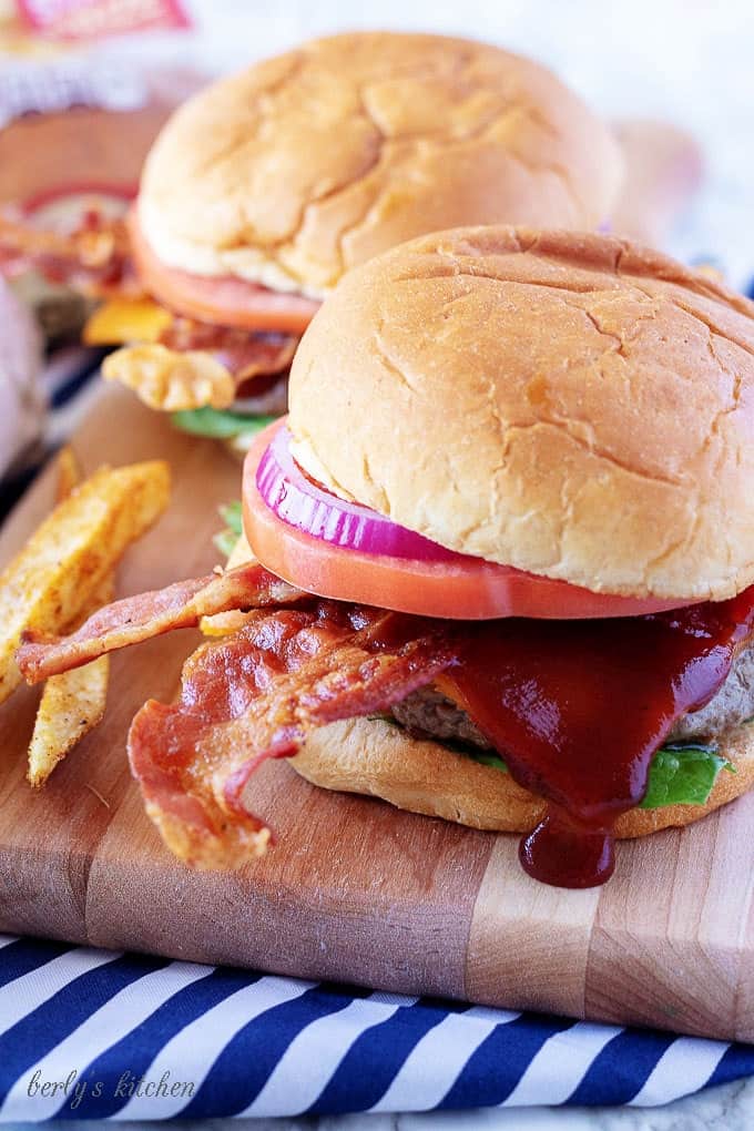 A close-up photo of the finished bacon cheeseburgers loaded with cheddar cheese, bbq sauce, and bacon.