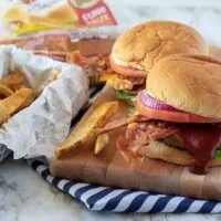 The finished bacon cheeseburgers on a cutting board, served with fries and BBQ sauce.