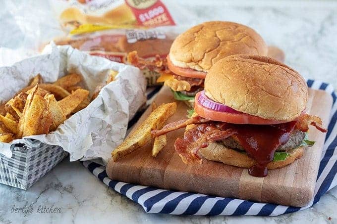 The finished bacon cheeseburgers on a cutting board, served with fries and bbq sauce.