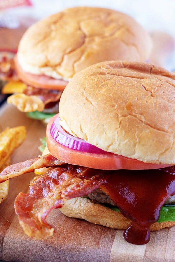 A close-up picture of the finished bacon cheeseburgers topped with cheese, bbq sauce, and bacon.