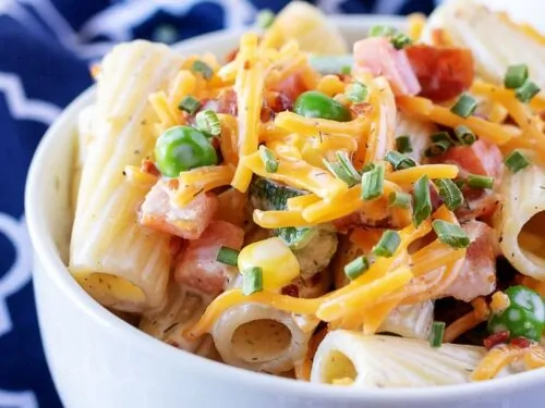 A close-up photo of the finished cold pasta salad with vegatbles, garnished with extra cheese and bacon.