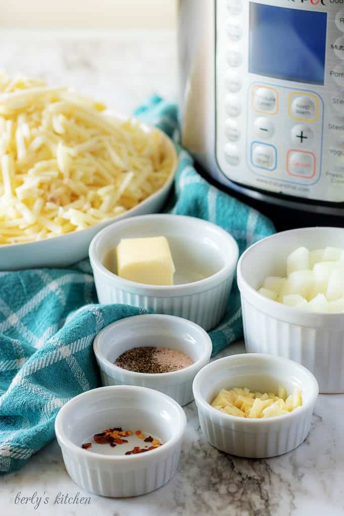 The funeral potatoes ingredients, like onions, butter, and hash browns, in white ramekins.