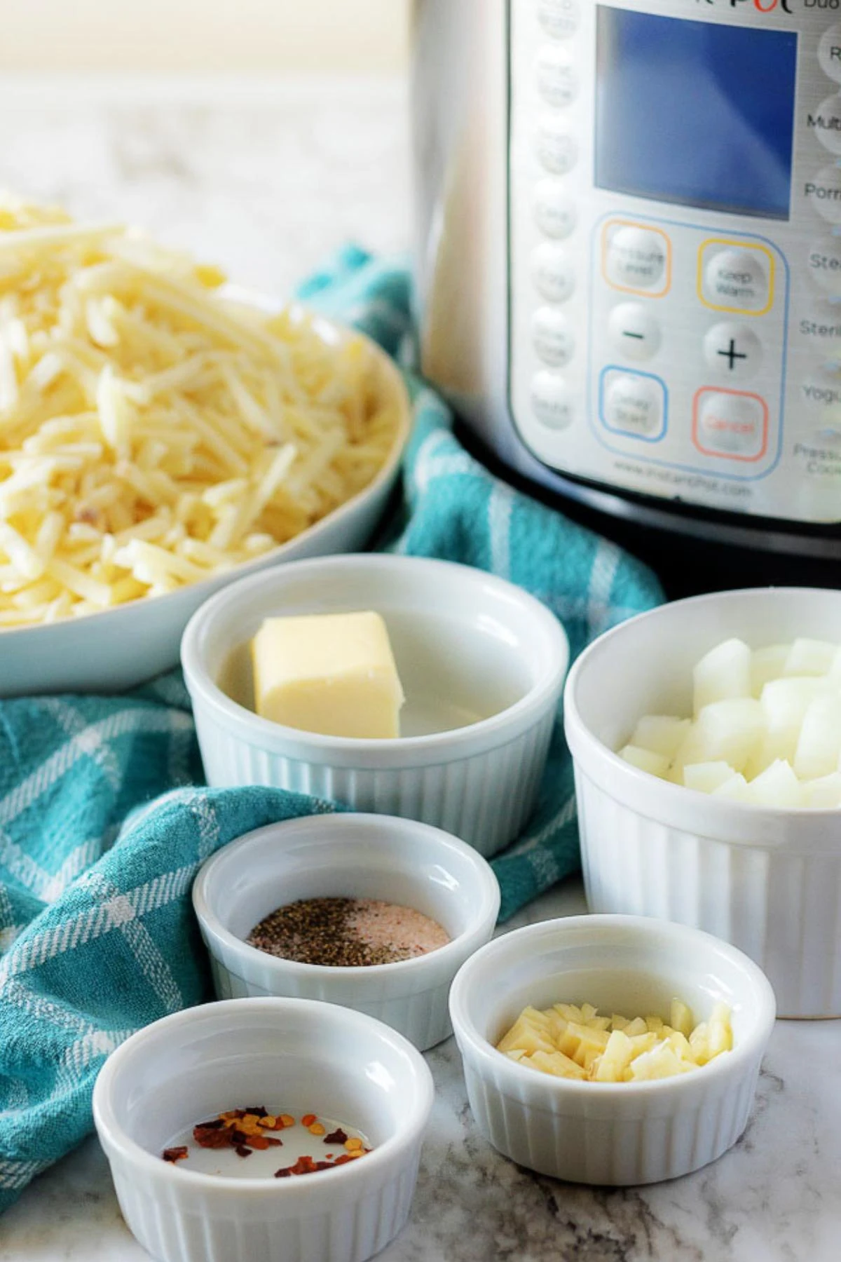 The funeral potatoes ingredients, like onions, butter, and hash browns, in white ramekins.