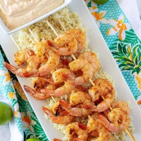 An aerial picture of the grilled shrimp skewers, over rice, with a square bowl of key lime aioli.