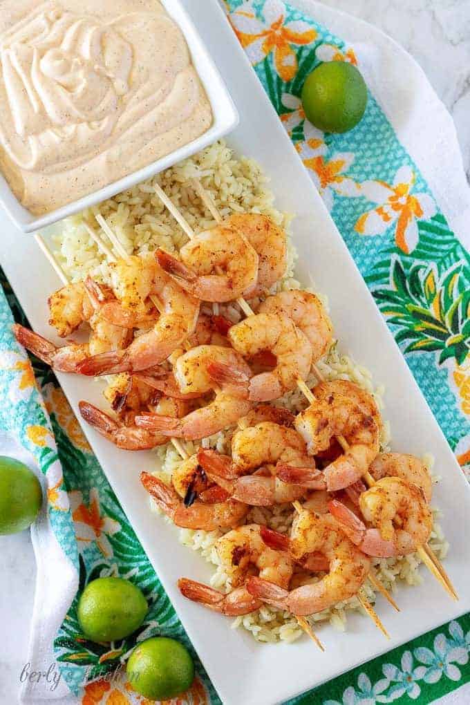 An aerial picture of the grilled shrimp skewers, over rice, with a square bowl of key lime aioli.