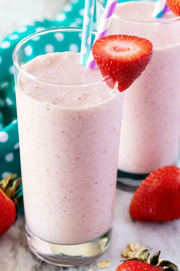 A close-up picture of the finished strawberry banana smoothies in glasses with straws and fresh strawberries.