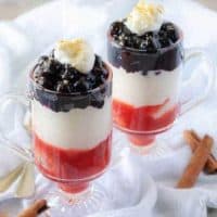 The finished blueberry cheesecake parfaits in mugs layered with strawberries, cheesecake, and blueberry toppings.