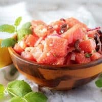 A small wooden bowl of watermelon salad, topped with fresh mint and crumbled feta cheese.