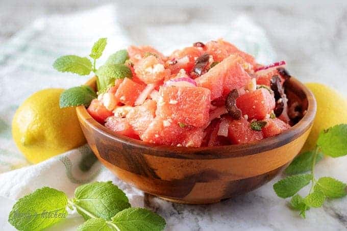 A small wooden bowl of watermelon salad, topped with fresh mint and crumbled feta cheese.