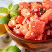 An angled photo of the watermelon salad in a small serving bowl loaded with onions, feta, and fruit.