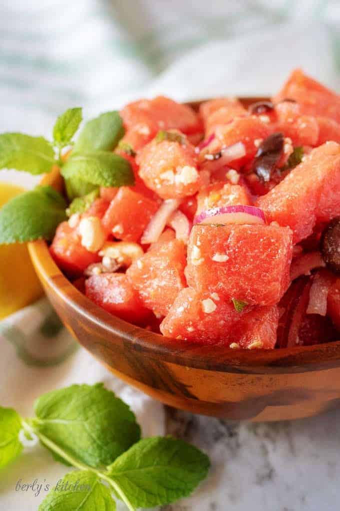 An angled photo of the watermelon salad in a small serving bowl loaded with onions, feta, and fruit.