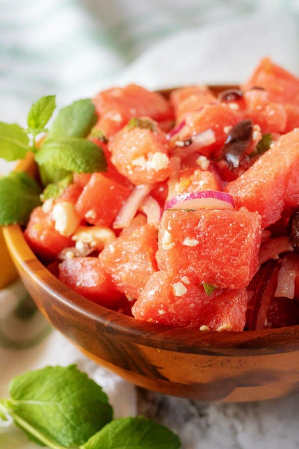 A close-up picture of the finished watermelon salad in a wooden serving bowl, garnished with mint.