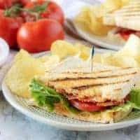 One half of the finished pimento cheese sandwich on grilled sourdough served with potato chips on white plate.