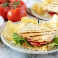 One half of the finished pimento cheese sandwich on grilled sourdough served with potato chips on white plate.