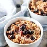 An aerial picture of the finished blueberry oatmeal garnished with fresh blueberries and heavy cream served in a white bowl.