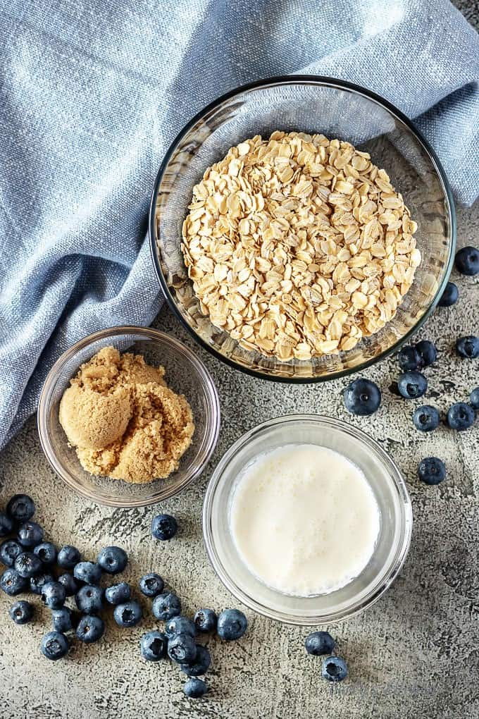 A top-down photo of the blueberry oatmeal ingredients like rolled oats, brown sugar, and fresh berries.