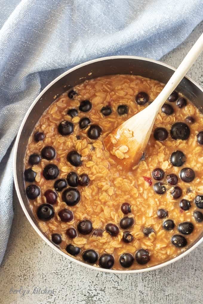 A picture of the blueberry oatmeal cooking in a medium saucepan with a wooden spoon in the center.