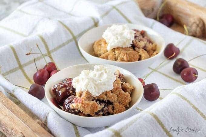 The finished cherry crisp in white bowls and topped with homemade whipped cream.