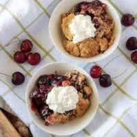 A top-down view of the cherry crisp in white bowls with whipped cream on top.