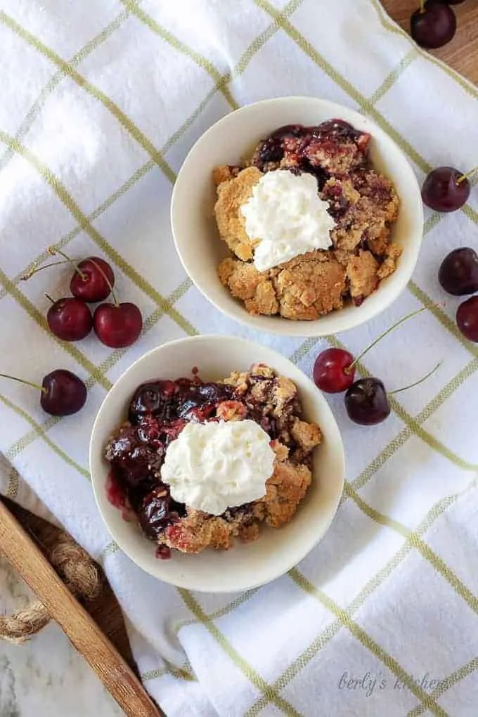 A top-down view of the cherry crisp in white bowls with whipped cream on top.