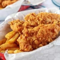 The homemade chicken tenders served with seasoned french fries served in red basket.