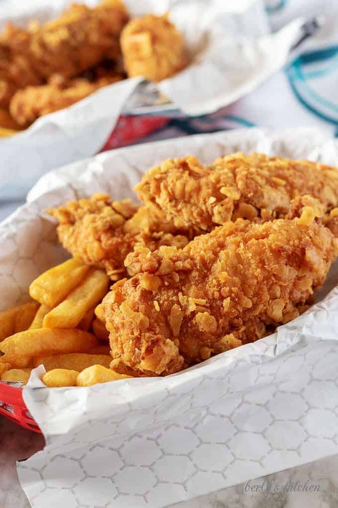 The homemade chicken tenders served with seasoned french fries served in red basket.