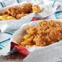The finished homemade chicken tenders in a red basket, with liner, served with french fries.