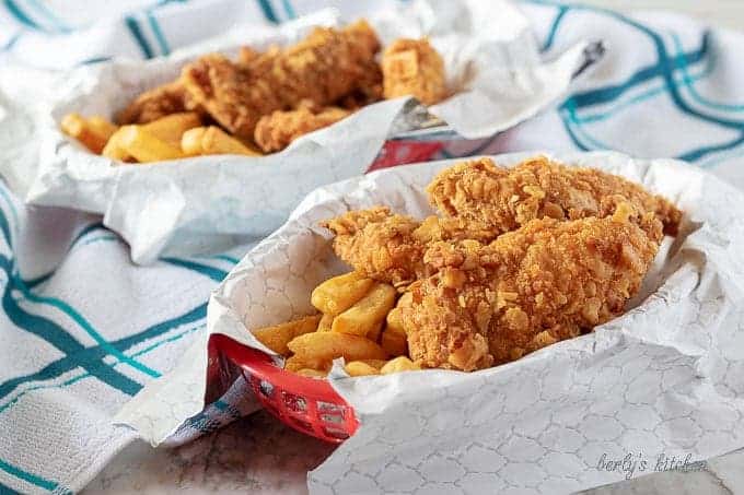 The finished homemade chicken tenders in a red basket, with liner, served with french fries.