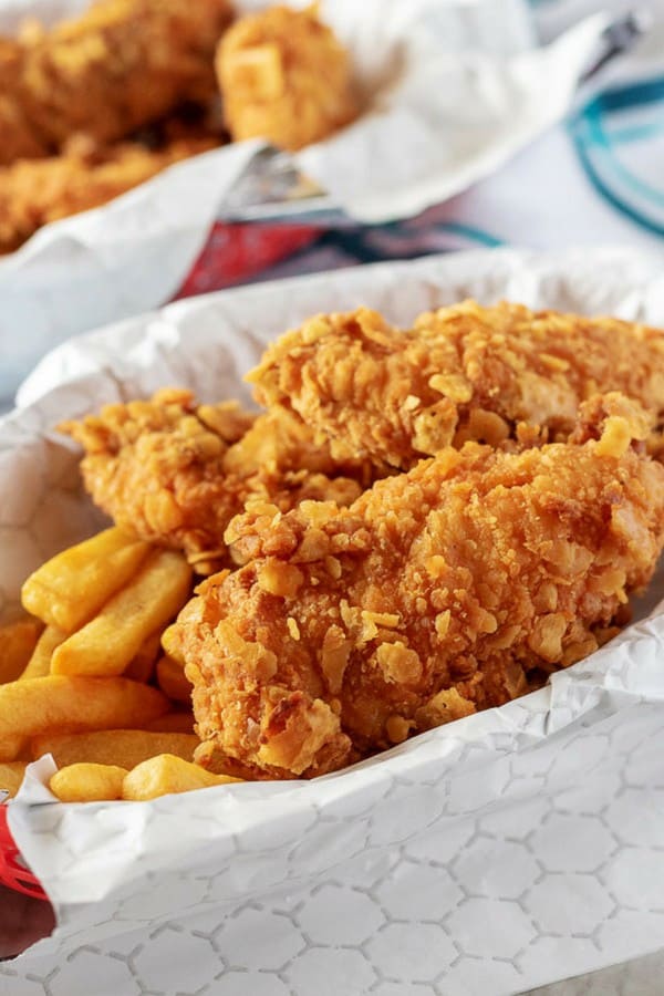 A close-up view of the homemade chicken tenders, served with fries, in a red basket with a white liner.