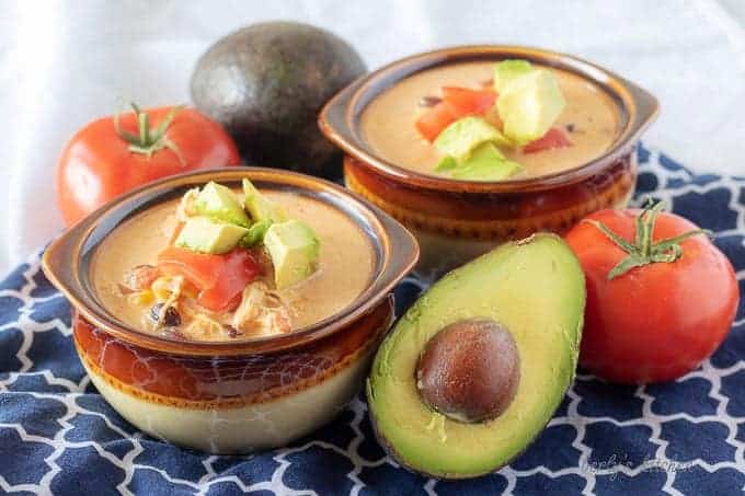 The finished chicken taco soup served in earthenware bowls and garnished with diced avocado and tomatoes.