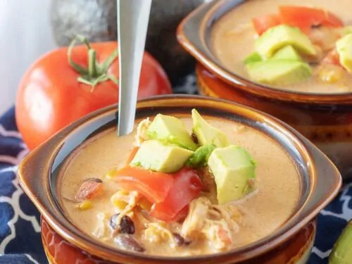 A close-up photo of the finished chicken taco soup in two earthenware bowls topped with diced tomatoes.