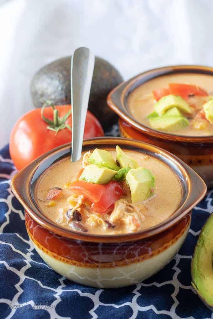 A close-up photo of the finished chicken taco soup in two earthenware bowls topped with diced tomatoes.