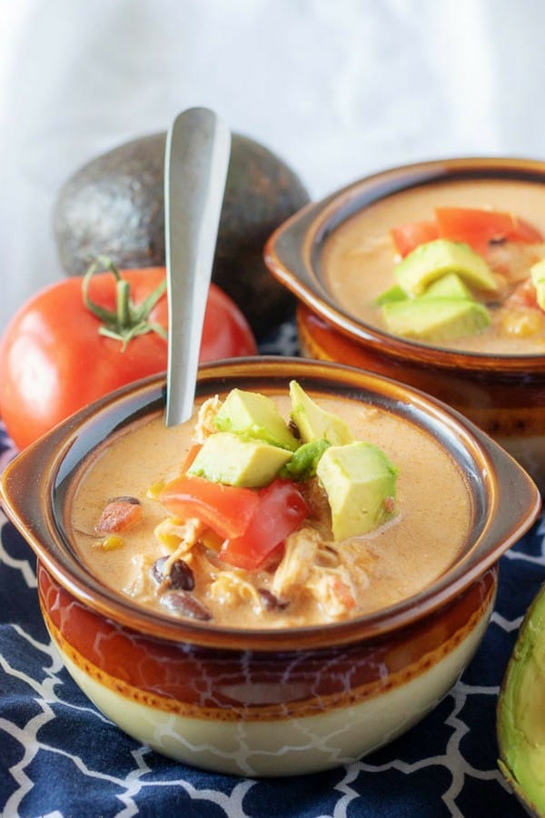 A large picture of the finished chicken taco soup in brown bowls and garnished with diced avocados and tomatoes.