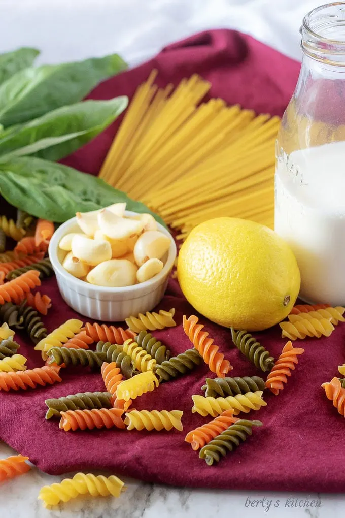 The lemon cream sauce ingredients, like fresh garlic and heavy cream with a fresh lemon surrounded by dry pasta.