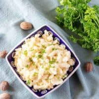 The finished spaetzle recipe in a square bowl, tossed in butter, and garnished with parsley.