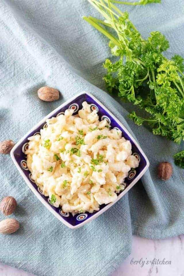 The finished spaetzle recipe in a square bowl, tossed in butter, and garnished with parsley.