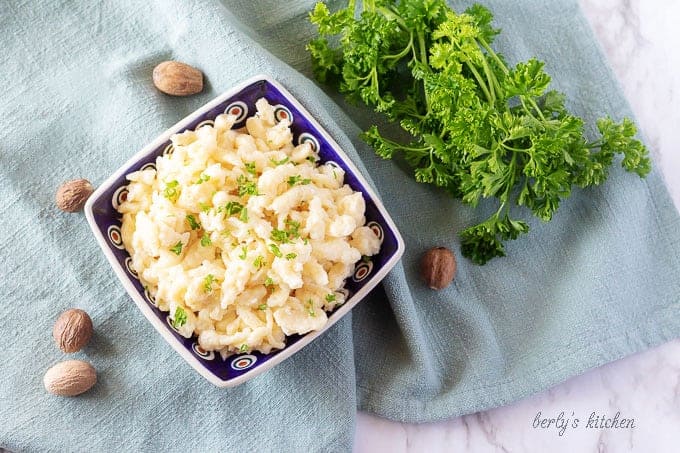 An aerial photo of the spaetzle recipe in a colorful blue bowl, garnished with parsley and ground nutmeg.