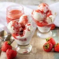 The finished bright red strawberry sauce drizzled over vanilla ice cream in stemless martini glasses.