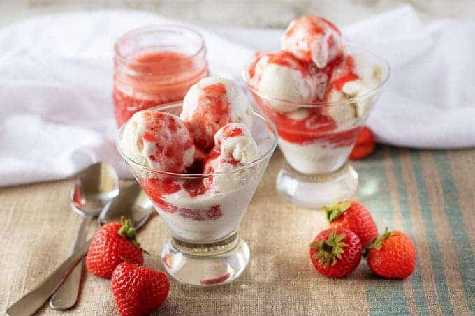 The finished bright red strawberry sauce drizzled over vanilla ice cream in stemless martini glasses.