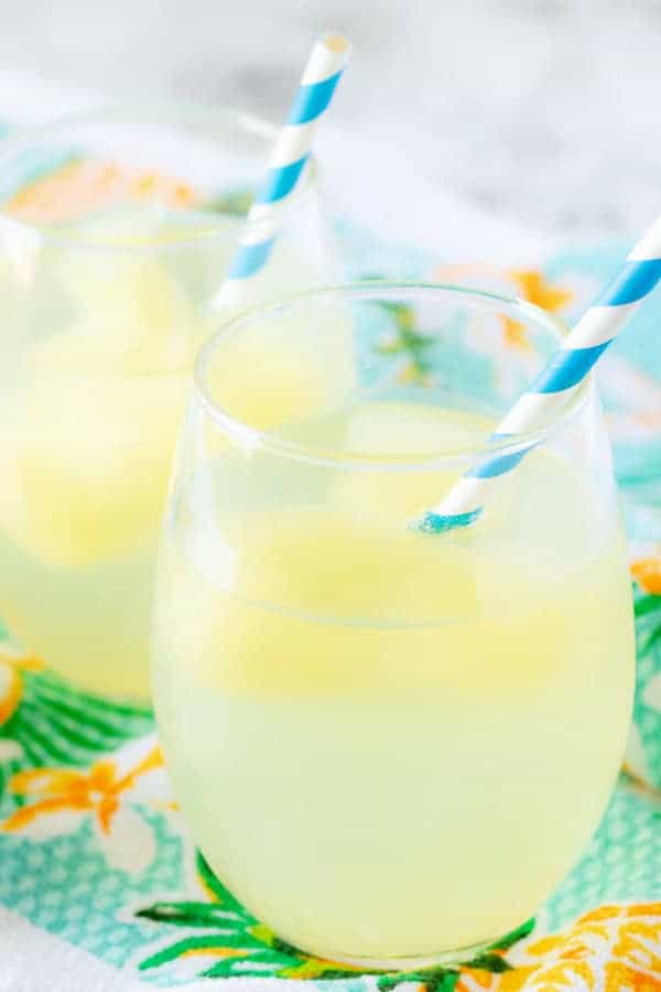 A close-up photo of the tropical cocktail booze cubes, melting in sparkling water, served in stemless wine glasses.