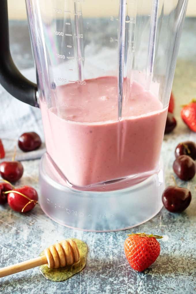 A side shot photo of the berry smoothie ingredients blended in a large clear blender.